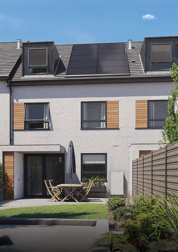 Reihenhaus mit Solarpaneelen, großer Terrasse, Garten und moderner Fassade bei blauem Himmel.